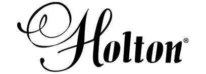 <p>Засновником американського бренду Holton, який зараз належить всесвітньо відомій музичній корпорації Conn-Selmer, Inc, був Френк Холтон. У кінці ХІХ сторіччя він грав на тромбоні, будучи головним тромбоністом оркестру Філіпа Сузи, автора національного маршу Америки. holtonІ ось на межі епох Френк Холтон розпочинає власну справу, що стає прообразом майбутньої компанії. Спочатку він стає власником музичного магазину в Чікаго, США. Окрім інструментів, що вже були у використанні, там можна було придбати і масло для тромбонів, виготовлене за його власним фірмовим рецептом. Доки справа розвивалася, весь вільний час Холтон і далі присвячував грі на тромбоні. А вже 1898 року Френк Холтон створив свій перший тромбон Holton Special. Минуло кілька років, і лінія Holton вже збагачувалася новими інструментами &ndash; підкорення музичного світу розпочали інші духові інструменти (труби, валторни, корнети). Вже 1914 року сам Вінсент Бах грав на трубі Holton у симфонічному оркестрі Бостона, ставши одним із видатних музикантів компанії. Крім Баха, як артисти Holton були відомі також корнетист Ernst Albert Couturier, тромбоніст Edward Llewellyn, трубач і музичний виробник Renold Otto Schilke, валторніст Філіп Фаркас (Philip Farkas), канадський геній джазу і трубач Мейнард Фергюсон (Maynard Ferguson), американський тубіст Харві Філліпс (Harvey Phillips) та інші музиканти. А співпраця компанії Holton з жінкою-піонером у грі на духових музичних інструментах, Kathryn Ethel Merker, призвела, серед іншого, до появи Holton Merker-Matic horn. Власну музичну фабрику Френк Холтон збудував у 1917&ndash;1920 роках у Елкхорні (штат Вісконсін, США). Виробництво розвивається шаленими темпами, швидко зростає кількість співробітників, майстрів, площі приміщень фабрики. 1929 року компанія робить новий крок у розвитку &ndash; з&rsquo;являється лінія Holton Collegiate, призначена для музикантів-початківців. 1939 Френк Холтон продав компанію Фреду Куллу своєму співпрацівнику та учню. А через три роки засновник помер. Подальший розвиток компанії, численні зміни у керівництві та зміни власників увінчалися входженням бренду Holton, який зараз вже називають живою легендою, до не менш популярної корпорації Conn-Selmer, Inc. Зараз духові інструменти Holton виробляються у Істлейку, штат Огайо (США).</p>