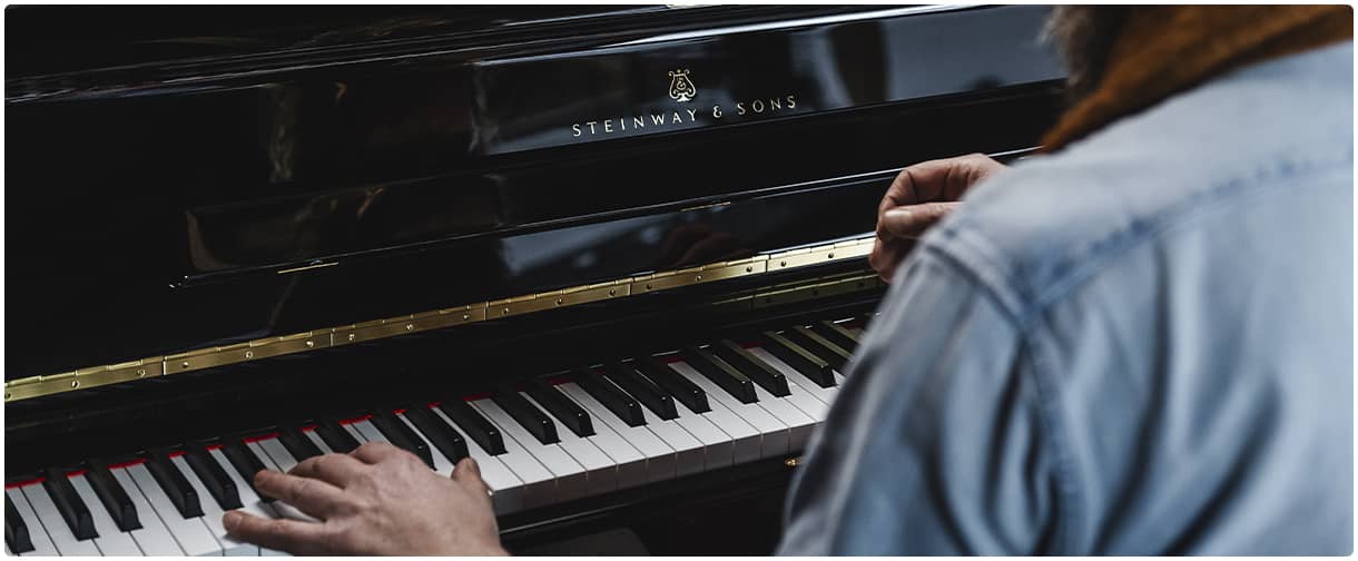 A man playing Steinway upright piano.
