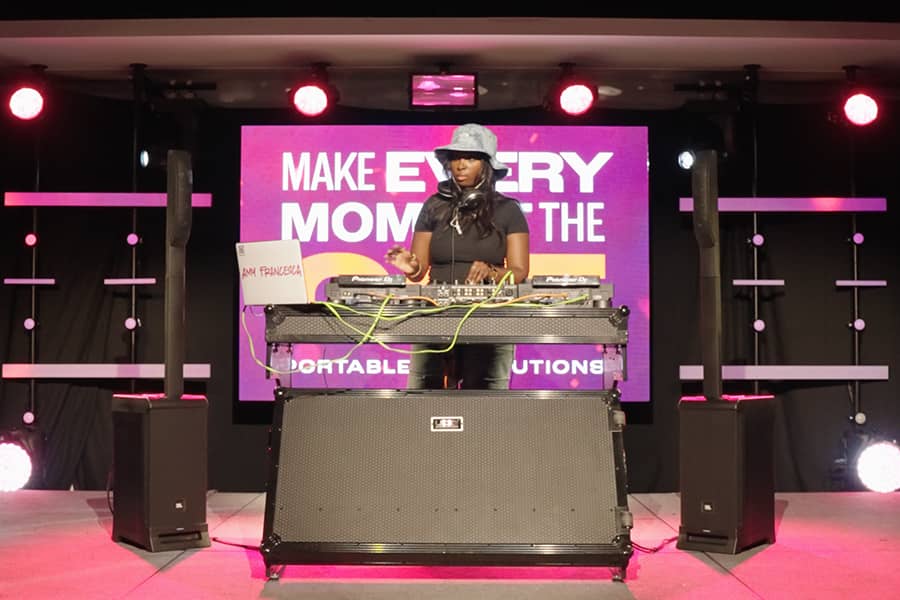 A DJ is standing on the stage with two JBL IRX ONE speakers.